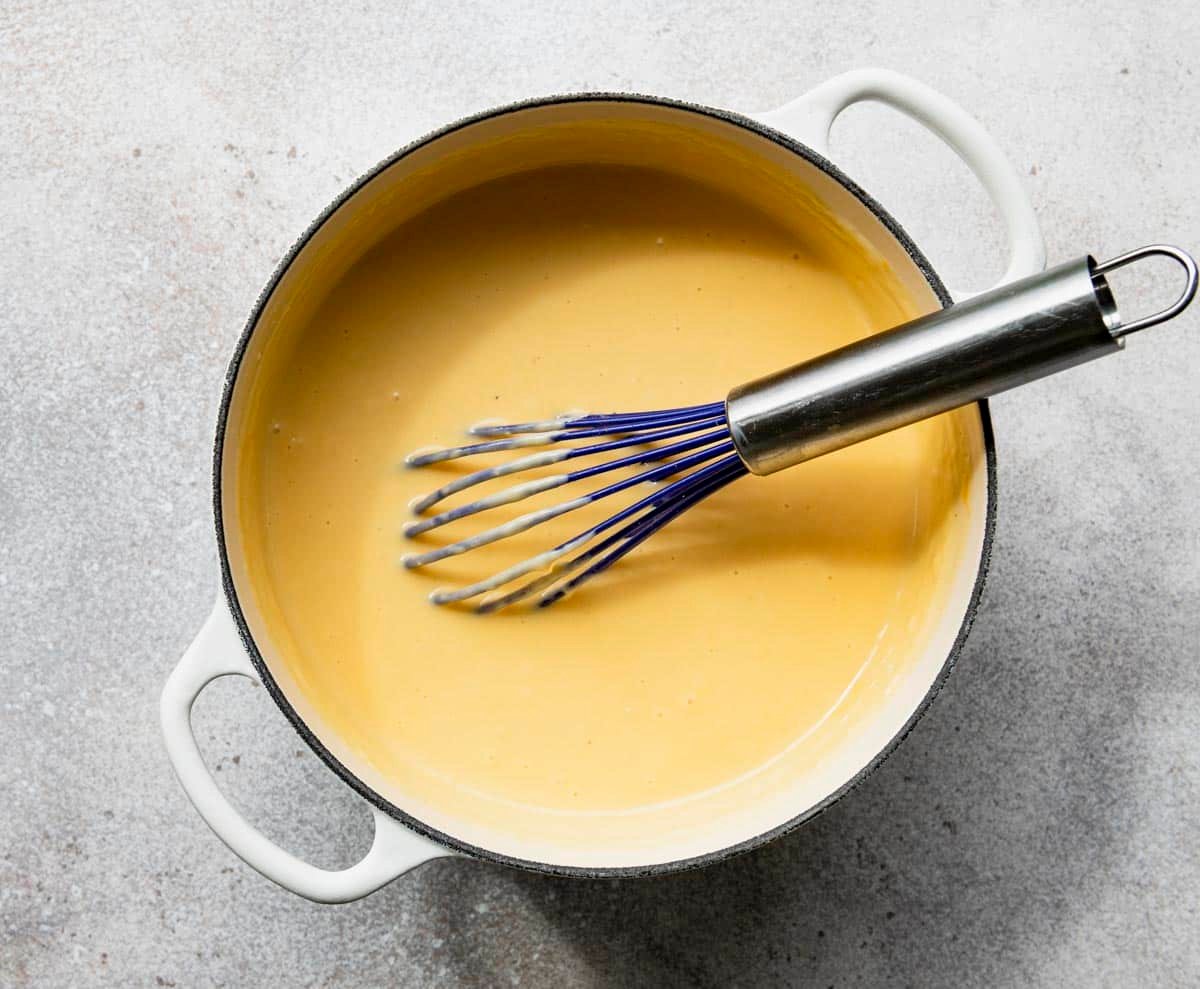 Whisking cheese sauce in a white Dutch oven.