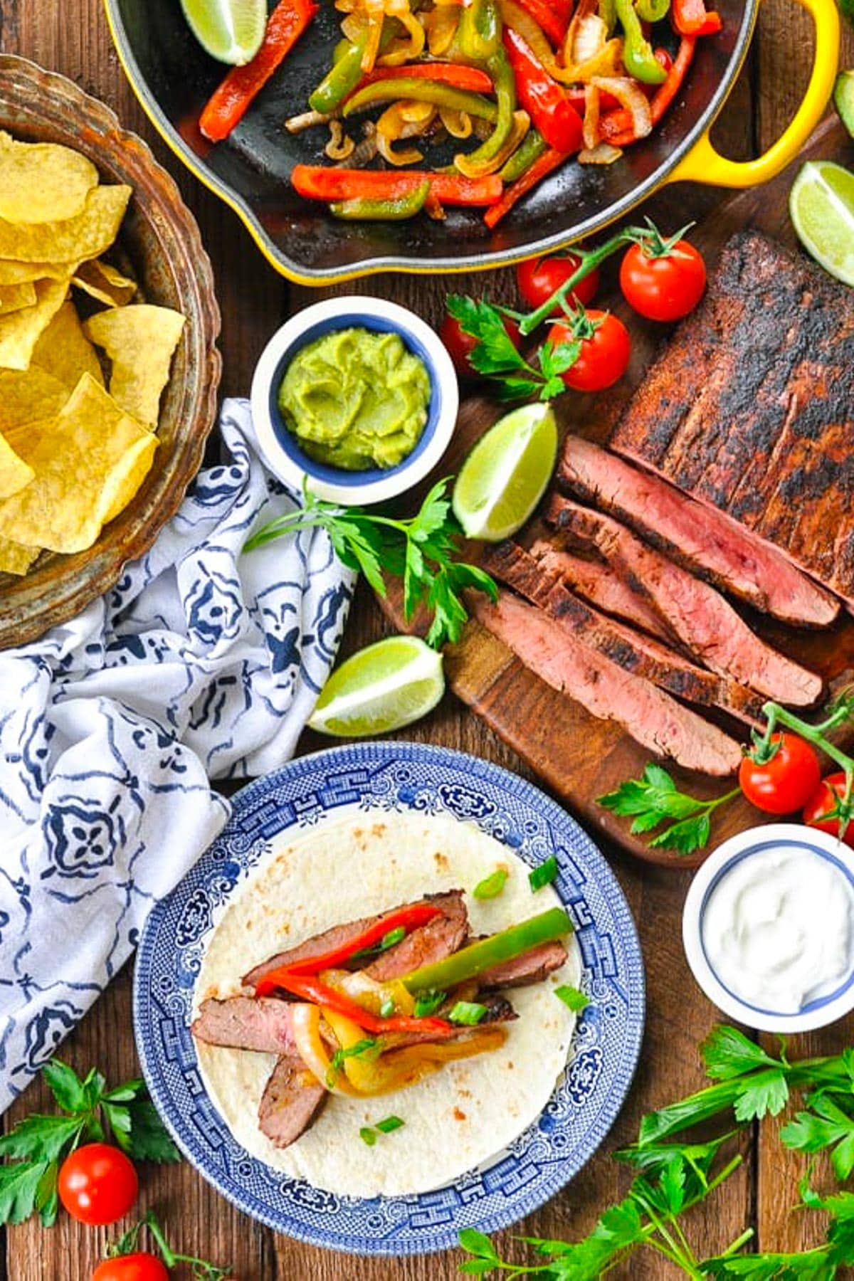Overhead image of grilled flank steak fajitas on a table with chips and guacamole on the side.