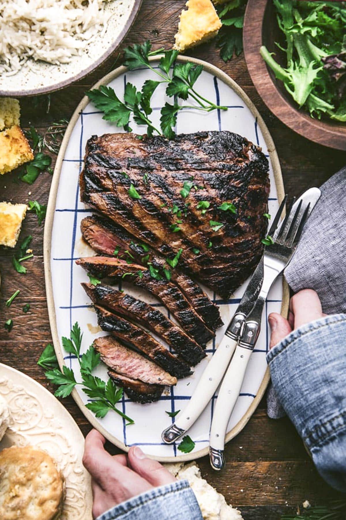 Hands serving a platter of marinated flank steak.