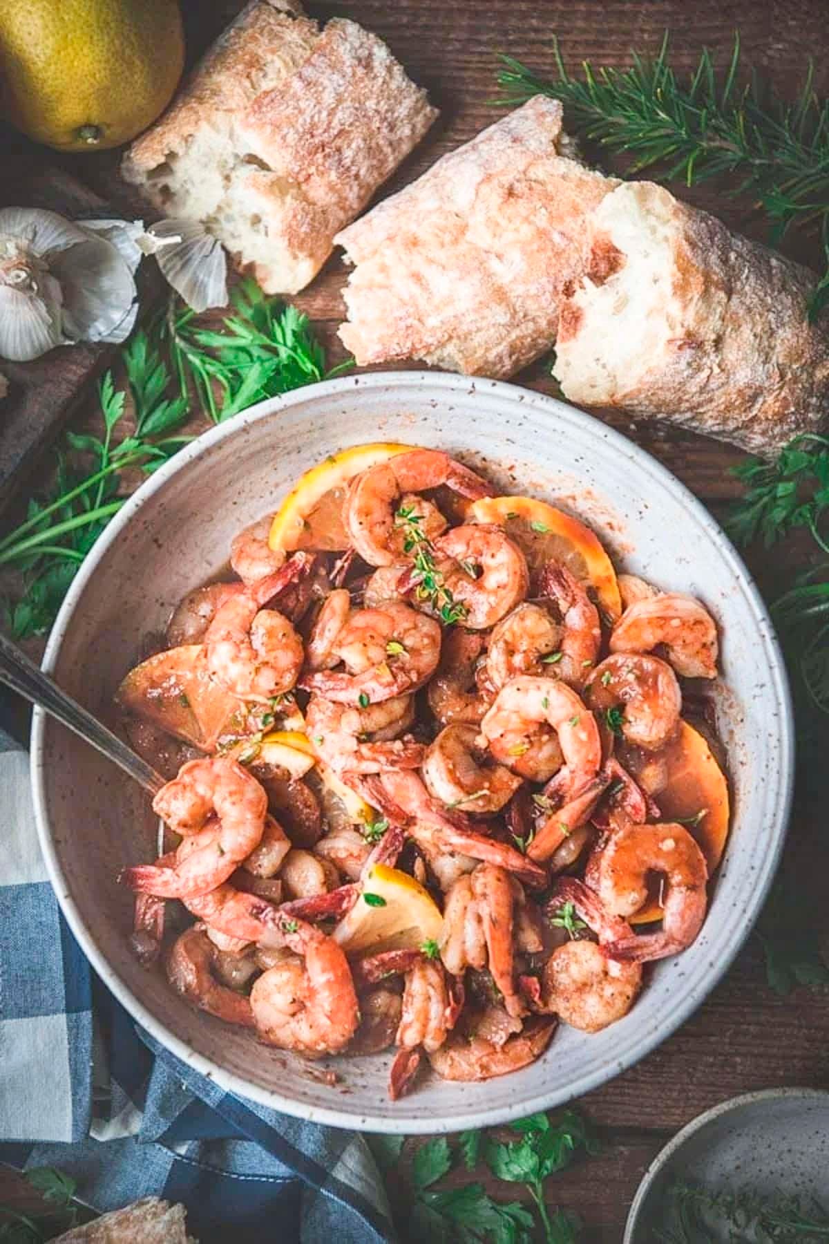 Overhead shot of garlic butter shrimp in a bowl on a wooden table with bread.