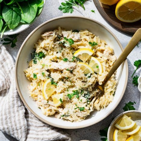 Square overhead shot of lemon chicken orzo in a white bowl with spinach and parmesan.