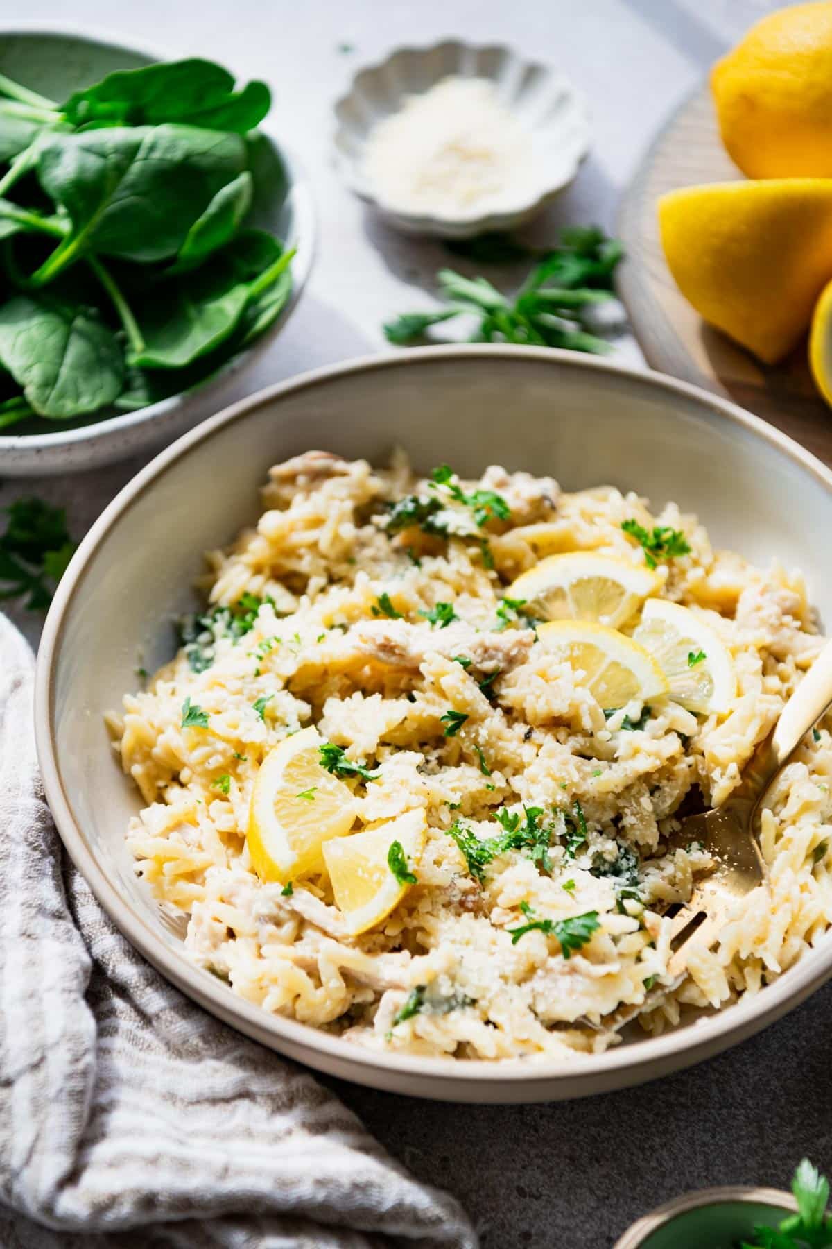 Side shot of creamy lemon chicken orzo in a white bowl with Parmesan on top.