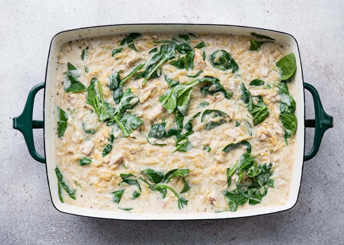 Lemon chicken orzo in a baking dish with fresh spinach added.
