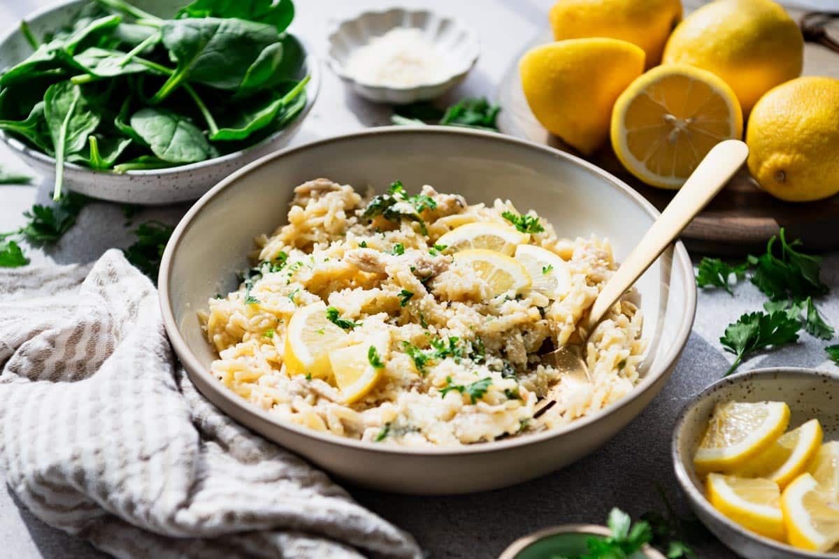 Horizontal side shot of a bowl of creamy lemon chicken orzo with spinach.