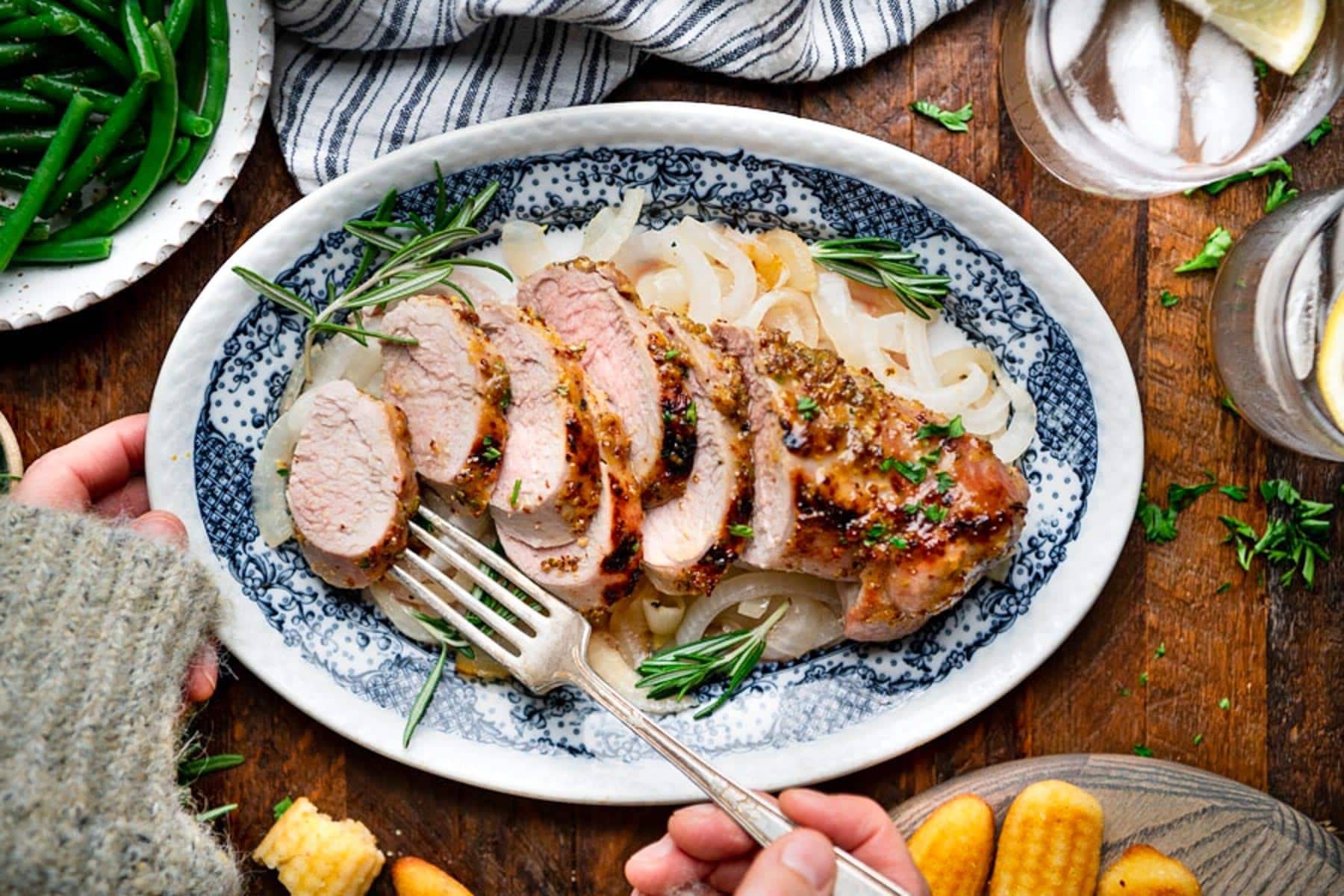 Overhead shot of an easy roasted pork tenderloin recipe served on a platter on a wooden dinner table with corn sticks.