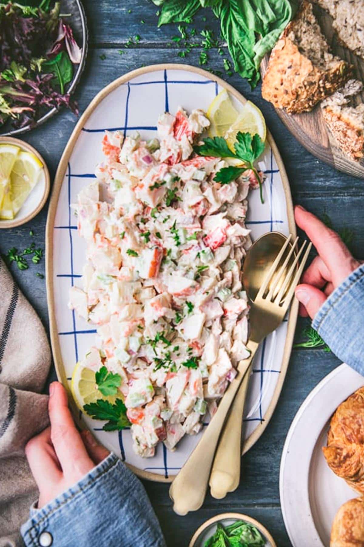 Overhead image of hands serving seafood salad on a blue and white tray.