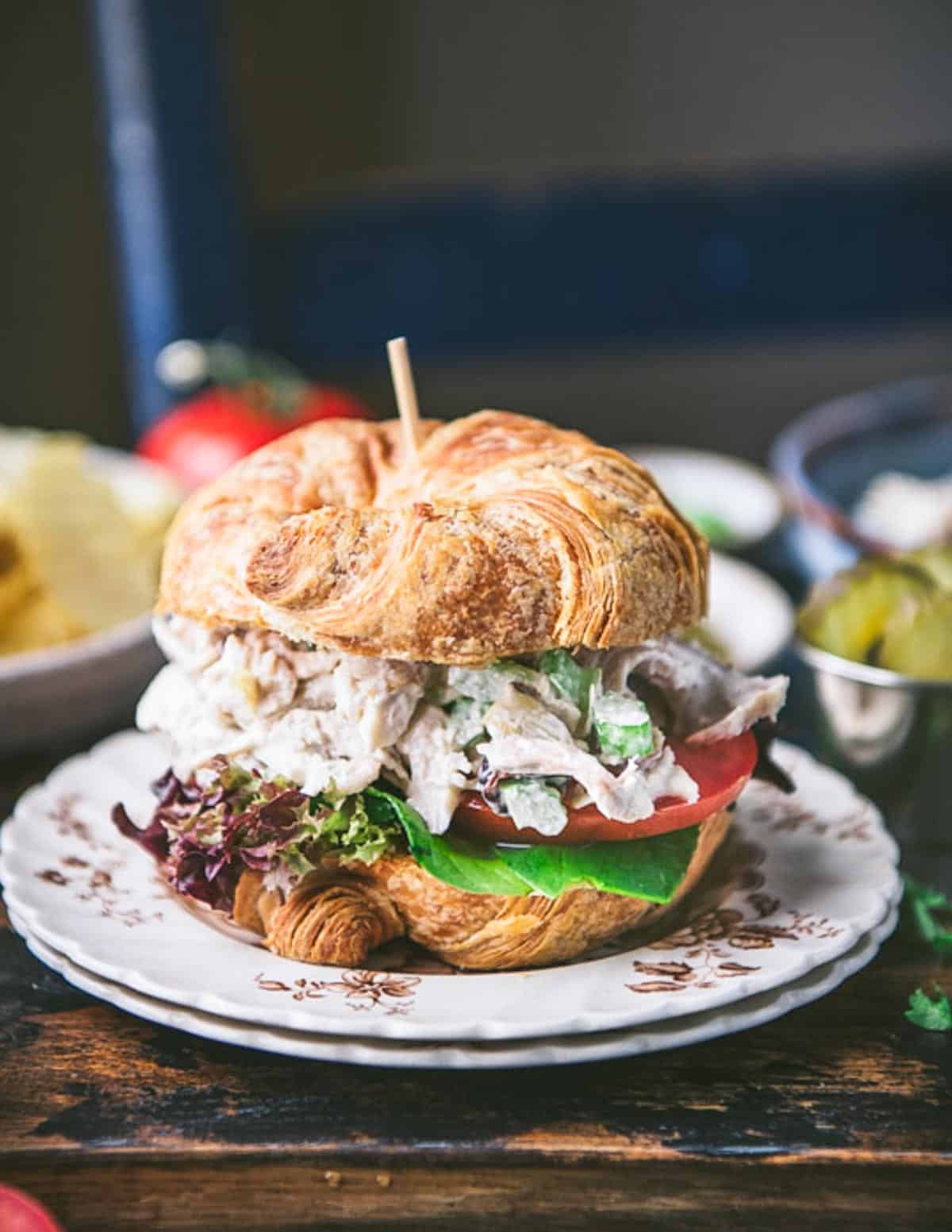 Side shot of a Southern chicken salad recipe served on a croissant sandwich on a rustic table.