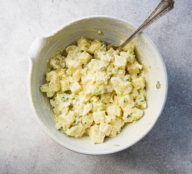 Process shot showing how to make a classic southern potato salad recipe in a white bowl.