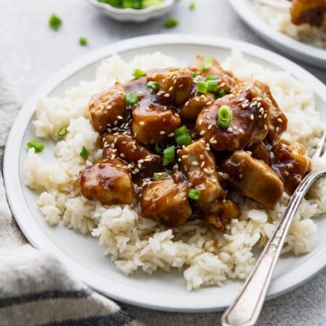 Close up square side shot of sticky chicken on a bed of white rice.