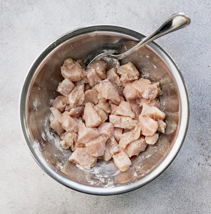 Diced chicken in a bowl tossed with cornstarch.