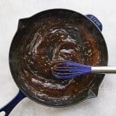 Whisking together sauce for sticky chicken in a cast iron skillet.
