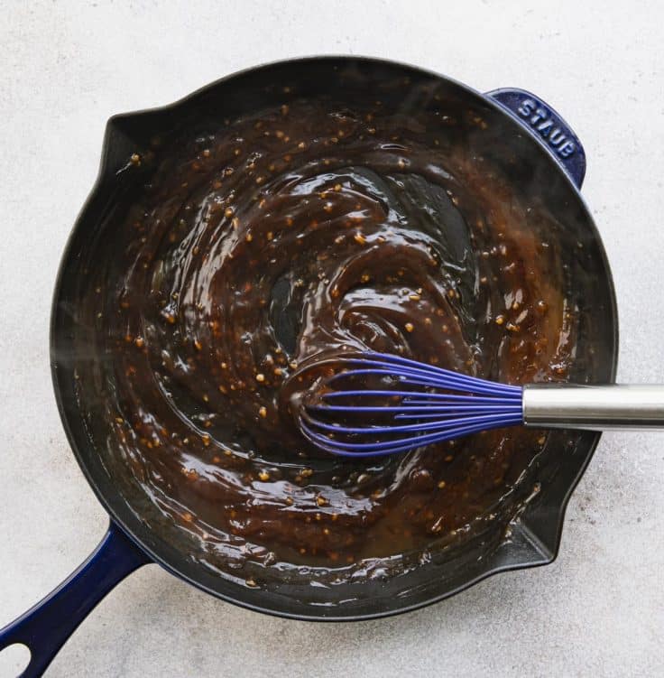Whisking together sauce for sticky chicken in a cast iron skillet.