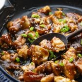 Sticky chicken in a cast iron skillet with a wooden spoon.