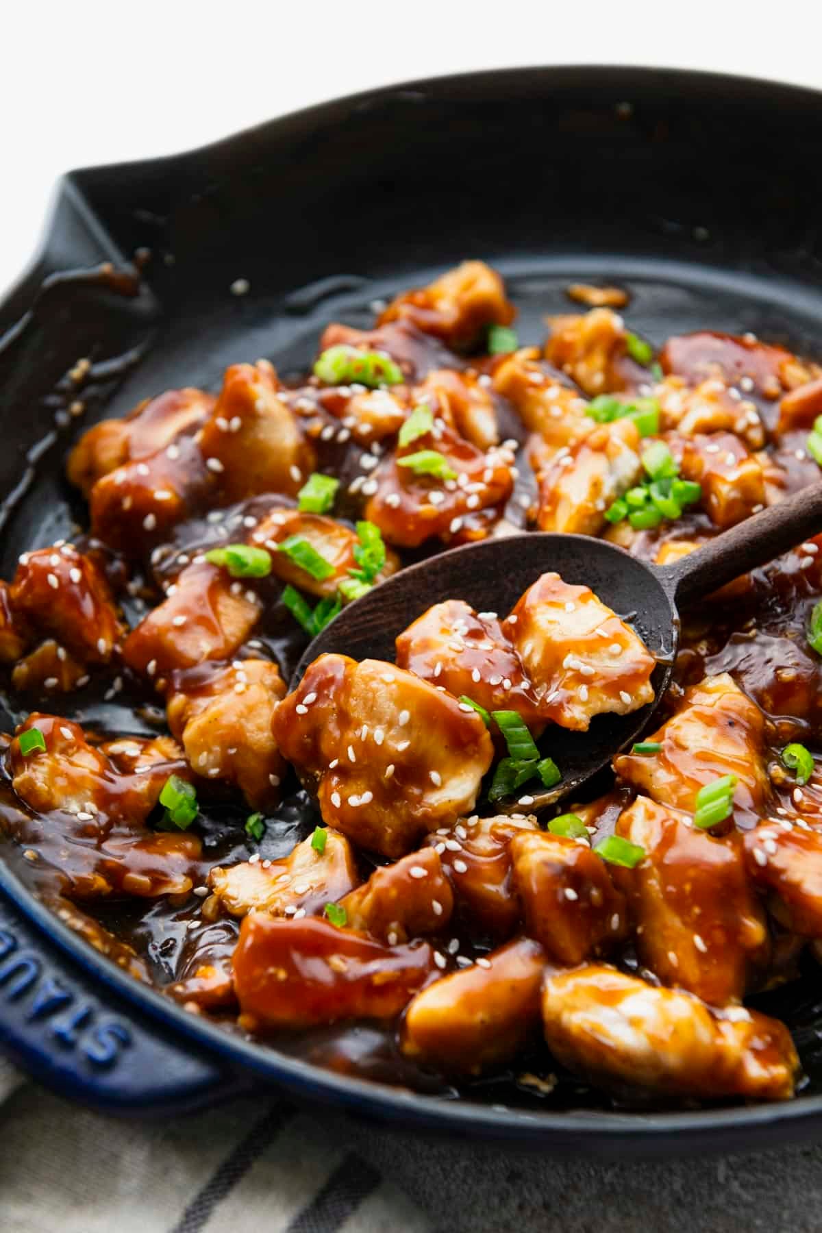 Sticky chicken in a cast iron skillet with a wooden spoon.