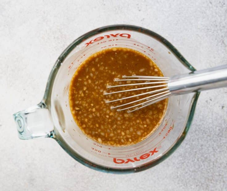 Whisking together sticky chicken marinade in a glass measuring cup.