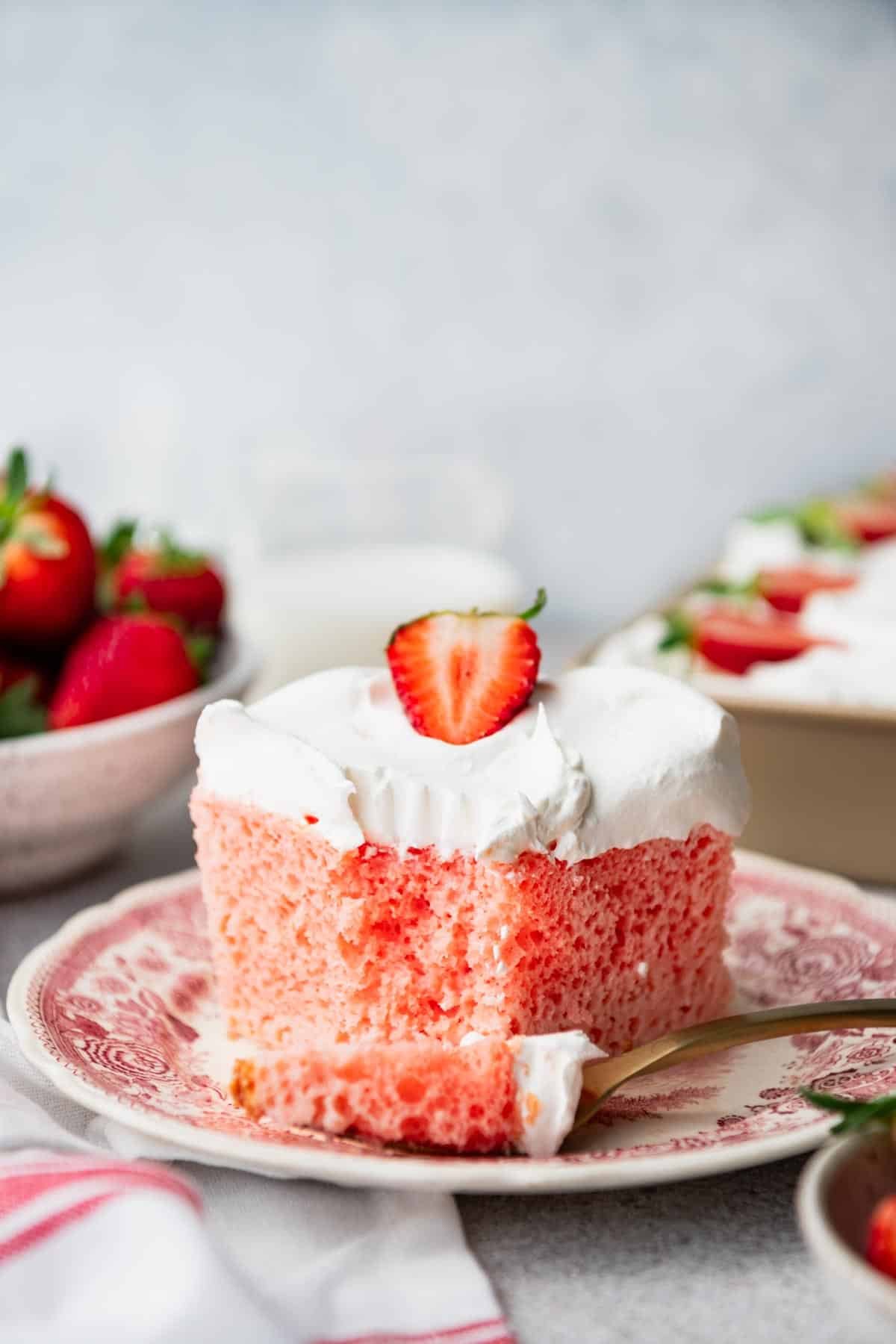 Close up front shot of a slice of strawberry tres leches cake on a red and white plate.