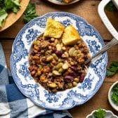 Square overhead shot of calico beans in a blue and white bowl with a side of cornbread.