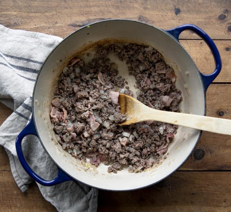 Browning ground beef, bacon, and onion in a cast iron dutch oven.