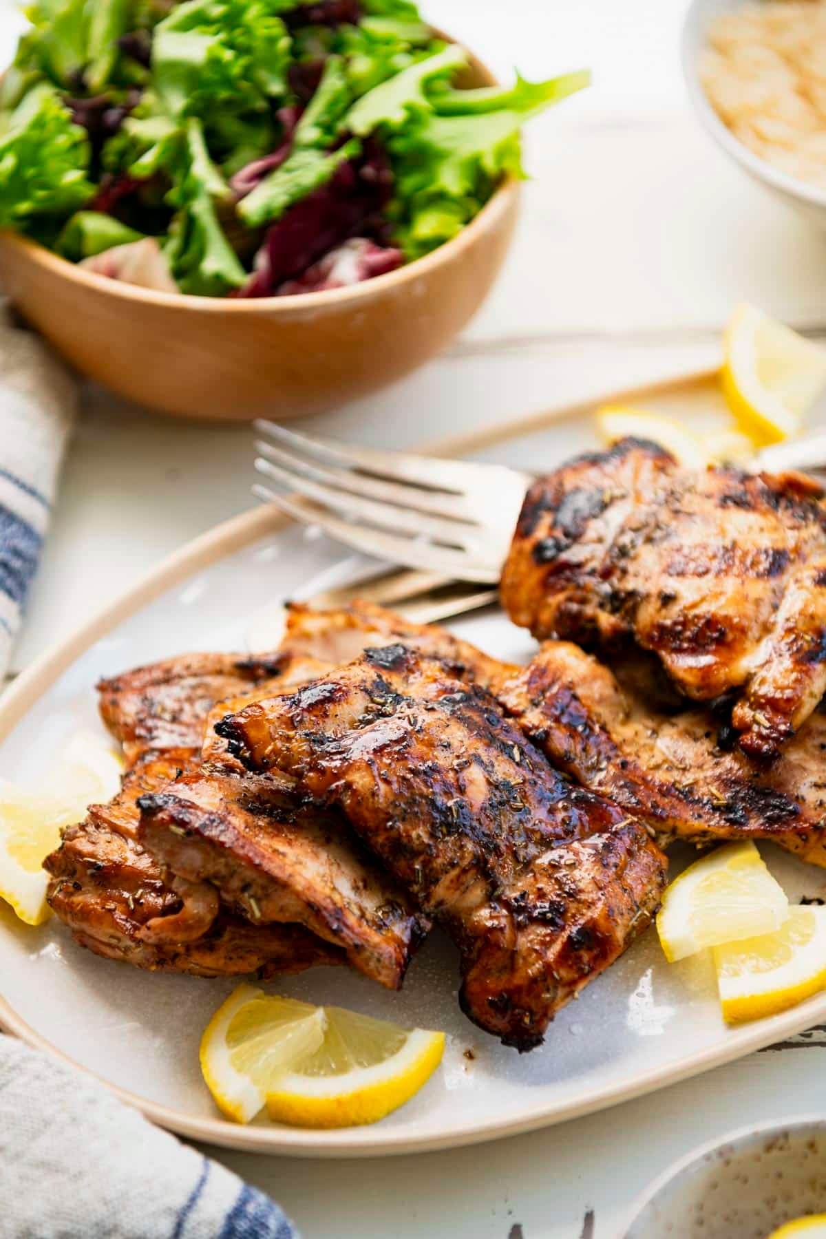 Close up shot of grilled marinated chicken thighs on a white tray with fresh lemons.