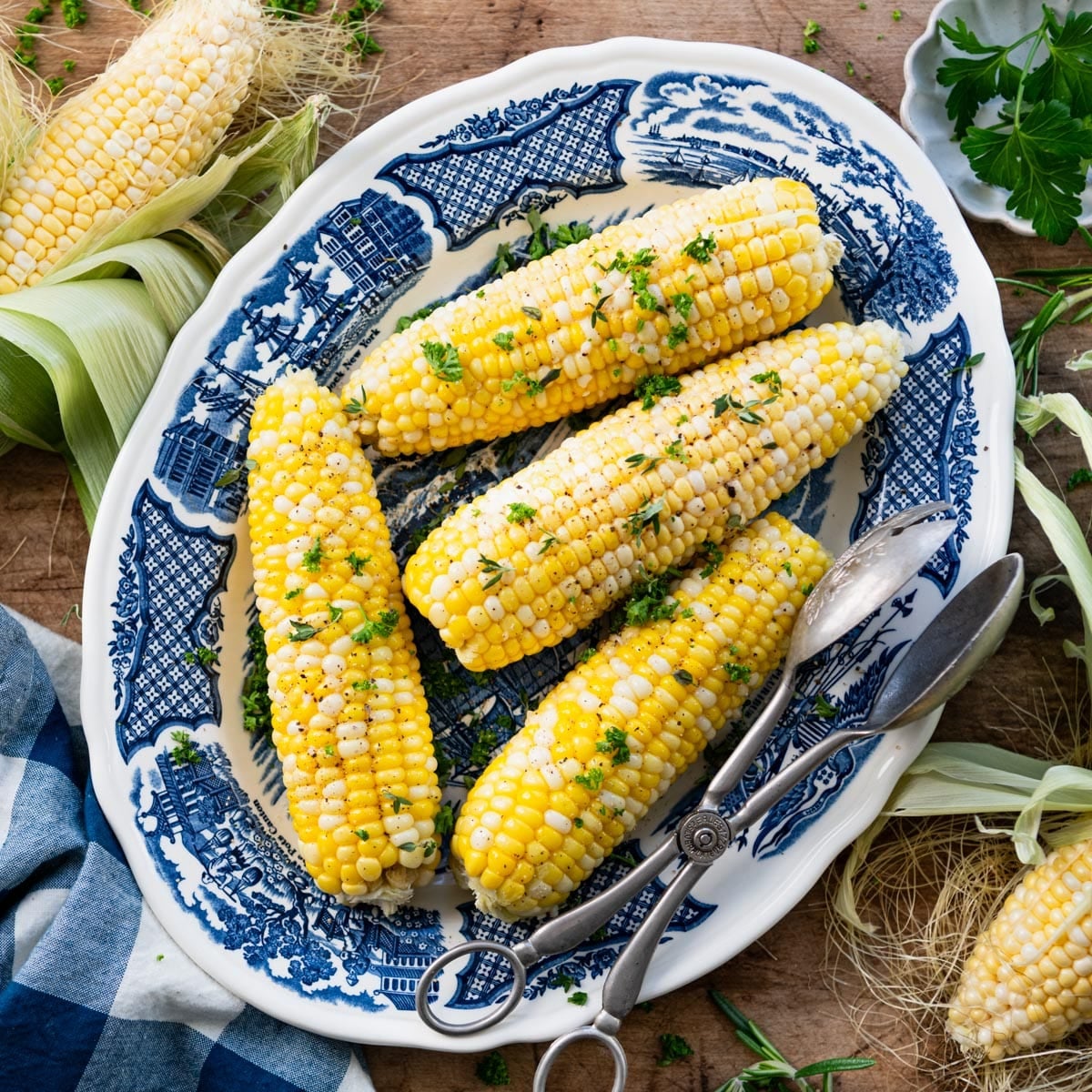 Square overhead shot of a corn on the cob in the oven served on a blue and white platter.