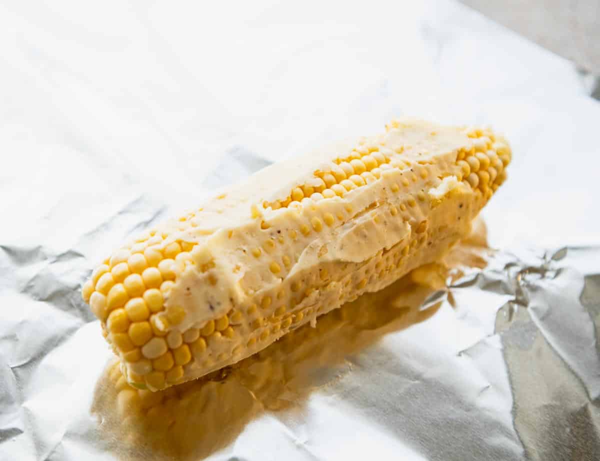 Spreading garlic butter on an ear of fresh corn.