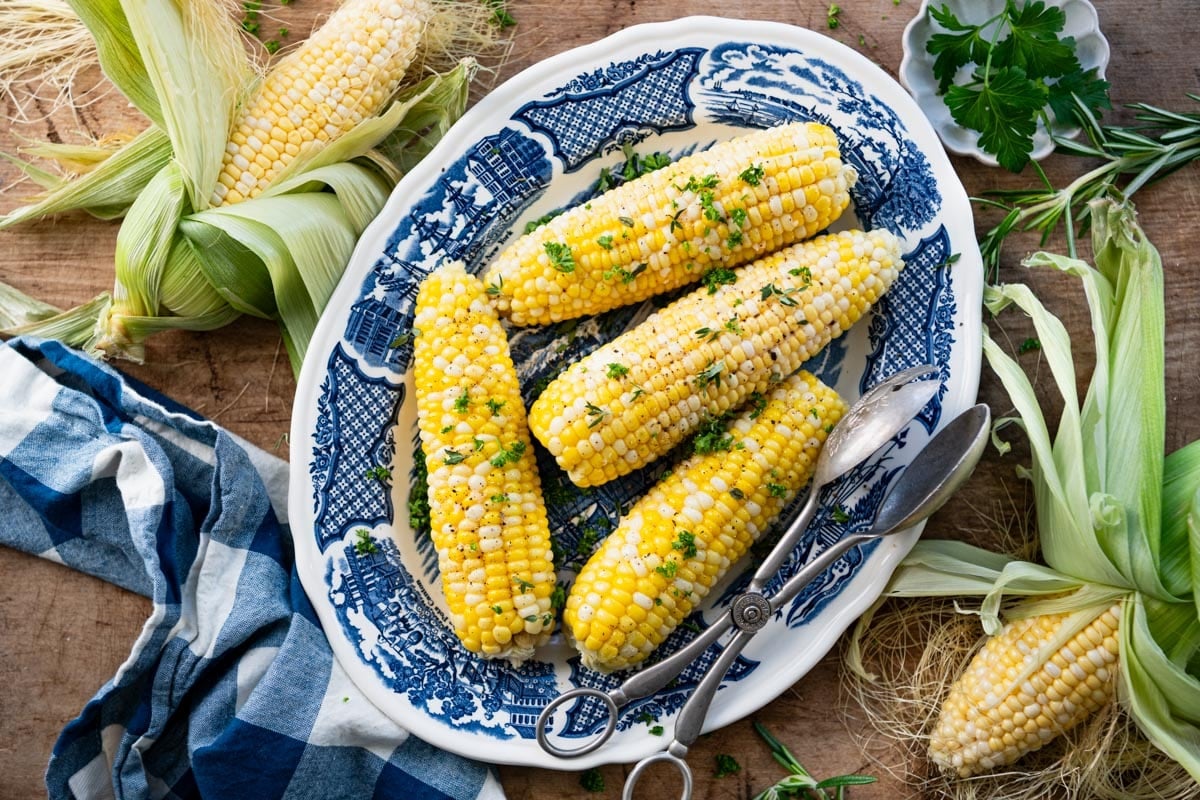 Horizontal overhead shot of corn on the cob in the oven and served on a blue and white plate.