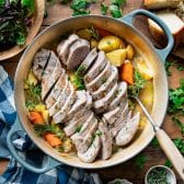 Square overhead image of a blue Dutch oven with pork tenderloin and vegetables.