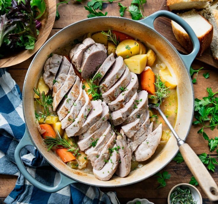 Square overhead image of a blue Dutch oven with pork tenderloin and vegetables.