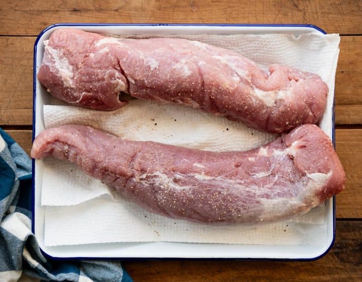 Two raw pork tenderloins on a white tray.