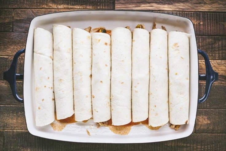 Rolled chicken enchiladas in a pan before adding the sauce and cheese on top.