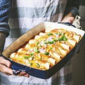 Close up square shot of a cook holding a pan of easy chicken enchiladas.