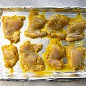 Chicken thighs in a golden marinade transferred to a baking sheet.