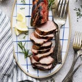 Square overhead shot of a marinated grilled pork tenderloin on a blue and white platter.