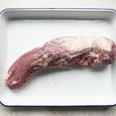 Pork tenderloin on a white tray seasoned with salt and pepper.
