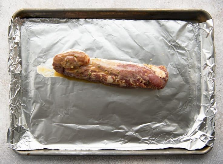 Overhead shot of pork tenderloin on a baking sheet after marinating.