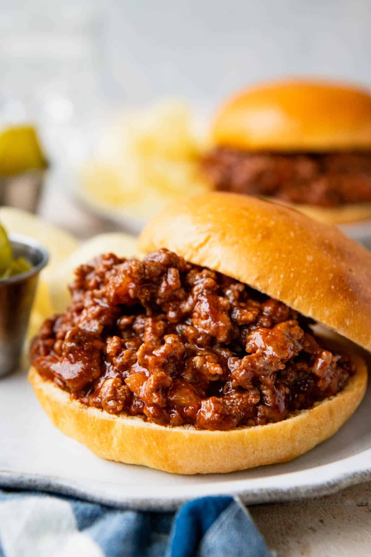 Side shot of old fashioned Sloppy Joes on a table with potato chips and pickles.