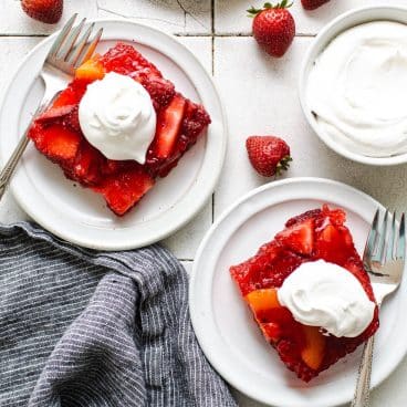 Square overhead shot of two white plates with strawberry jello salad.