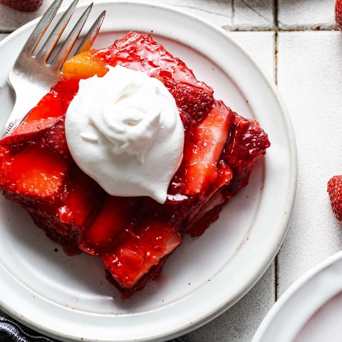 Square image of strawberry jello salad on a white plate.