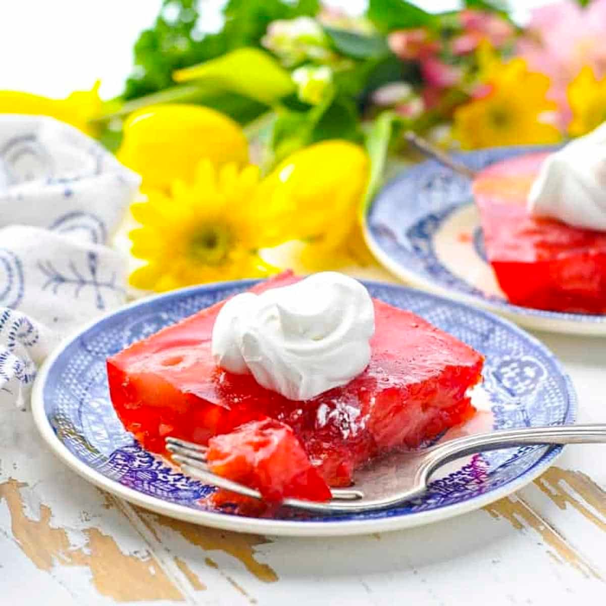 Square side shot of a slice of strawberry jello salad with cool whip on top.
