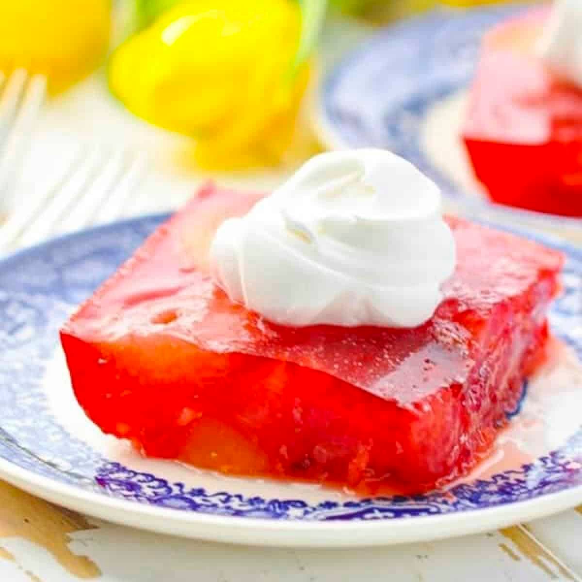 Square side shot of a slice of strawberry jello salad on a blue and white plate.