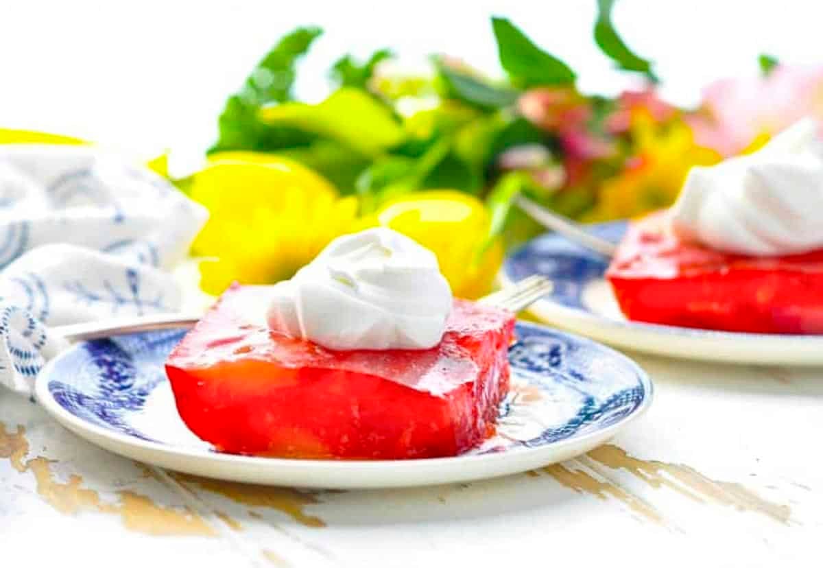 Horizontal side shot of strawberry jello salad on blue and white plates with flowers in the background.