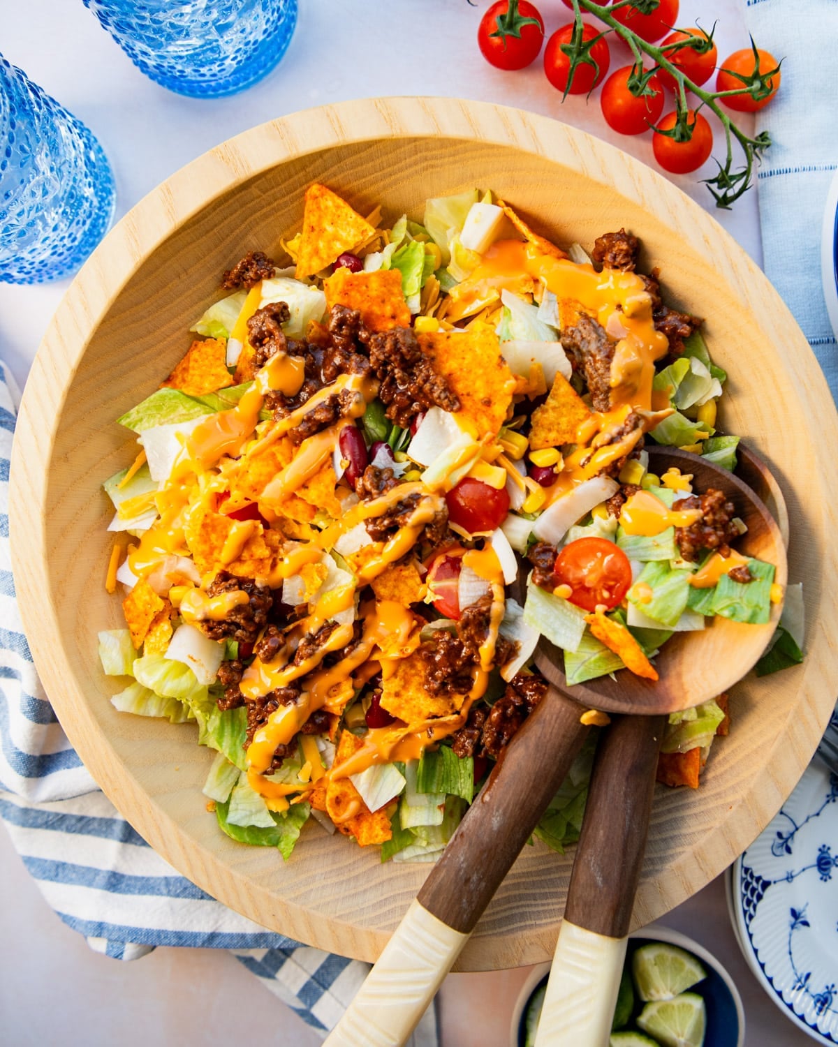 A big Dorito taco salad in a wooden salad bowl on a white table.