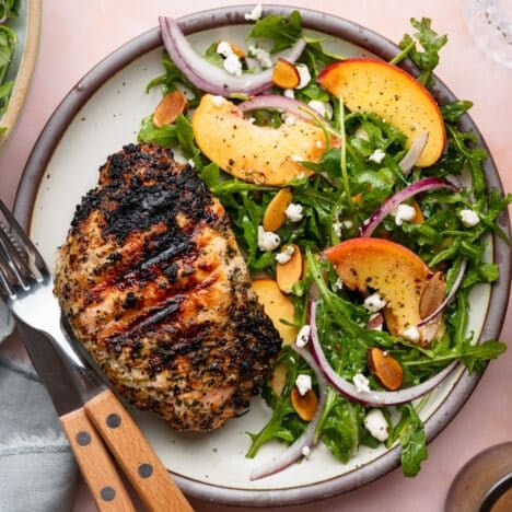 Square overhead shot of a grilled pork chop on a plate with a peach side salad.