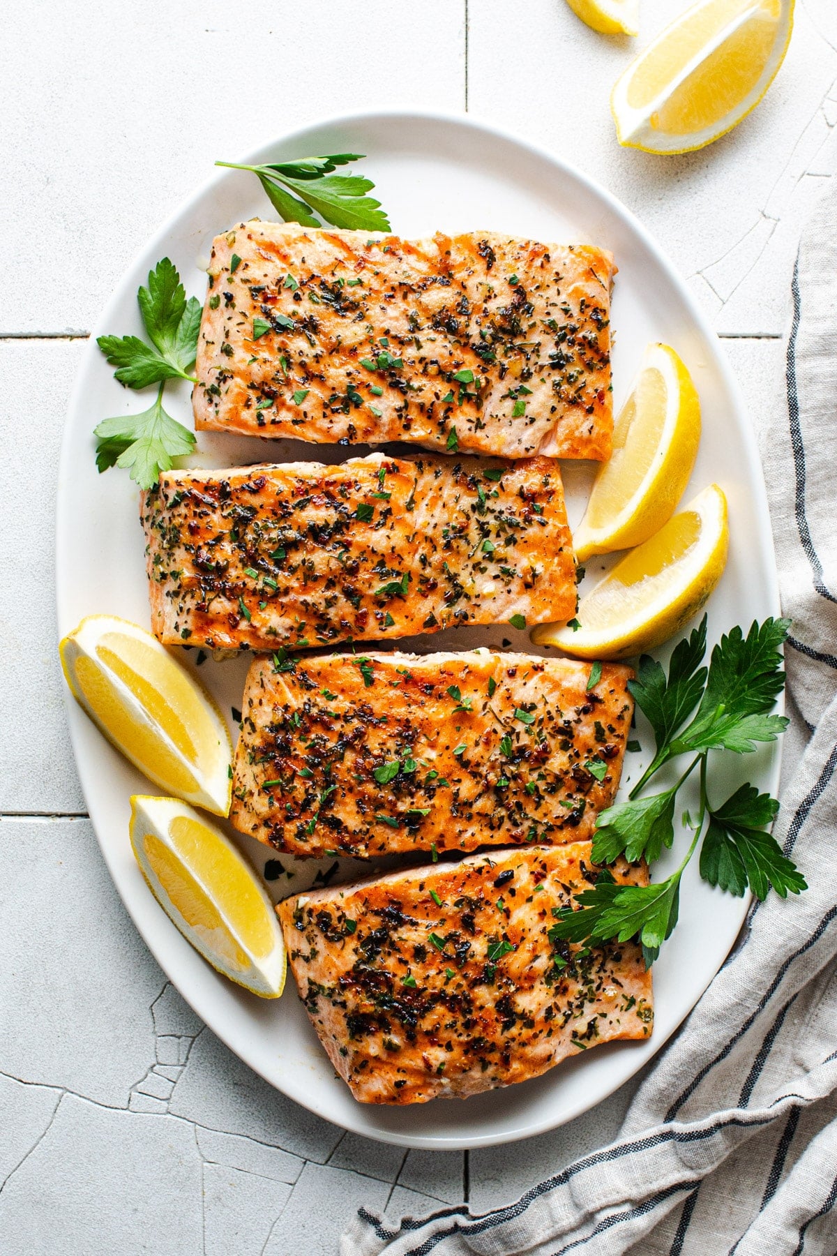 Grilled salmon fillets on a white serving platter with lemons and fresh parsley.
