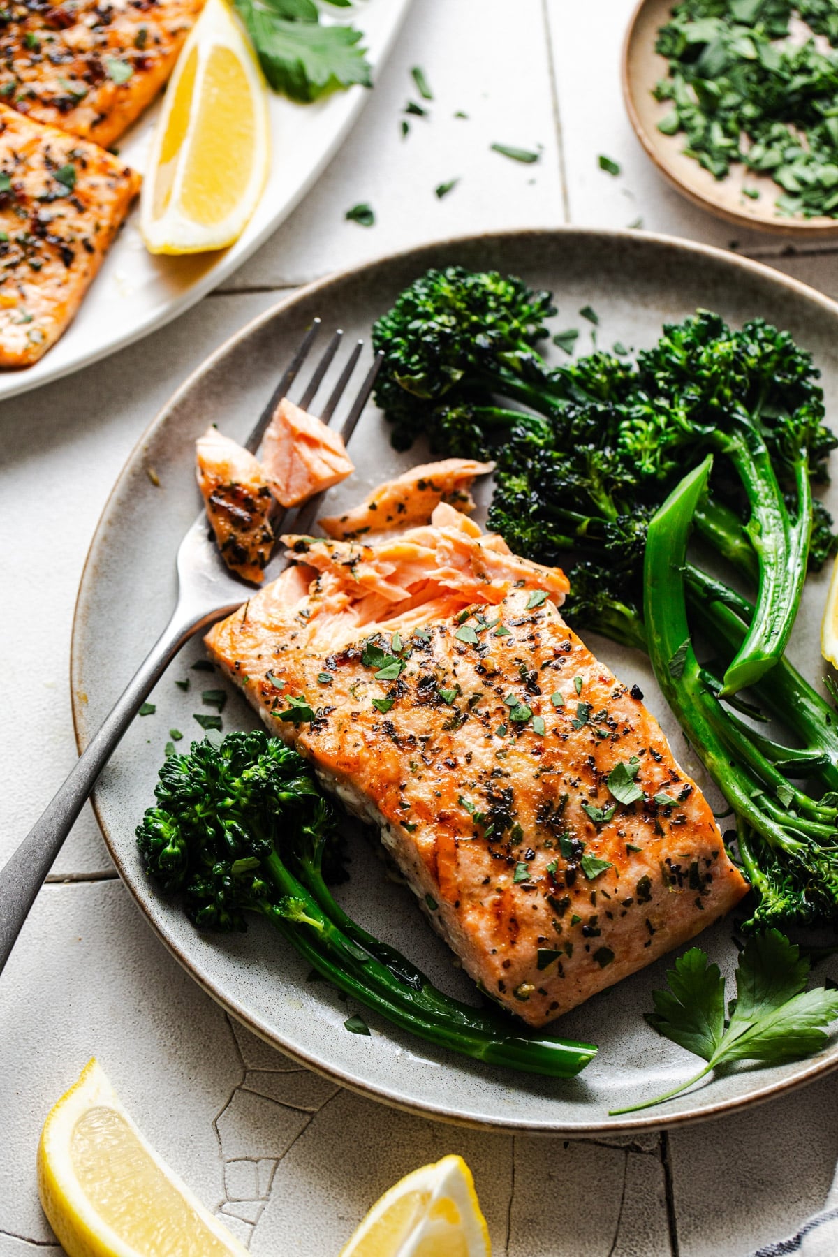 Bite of grilled salmon fillet on a fork on a plate.