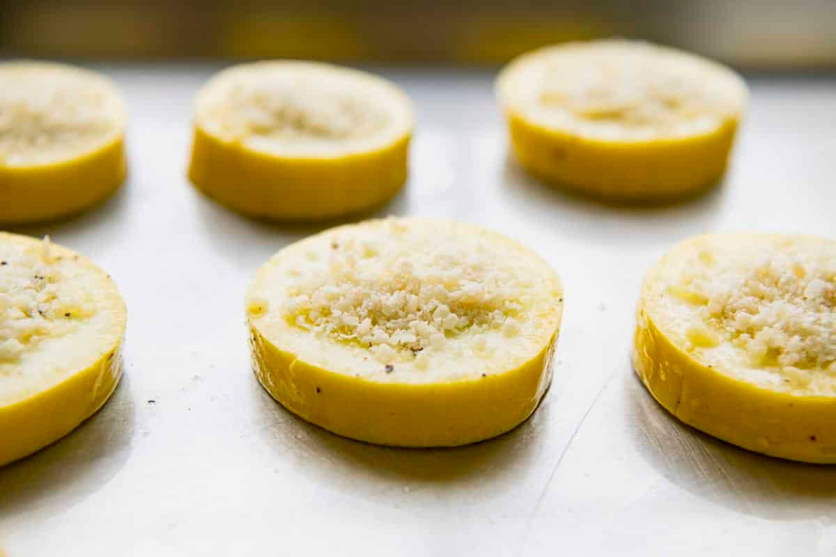 Parmesan cheese on top of yellow squash rounds on a baking sheet.