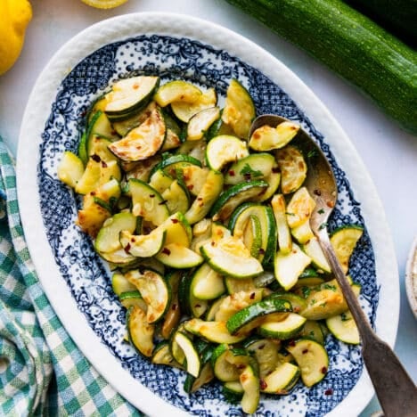 Square overhead shot of sauteed zucchini on a blue and white serving platter.