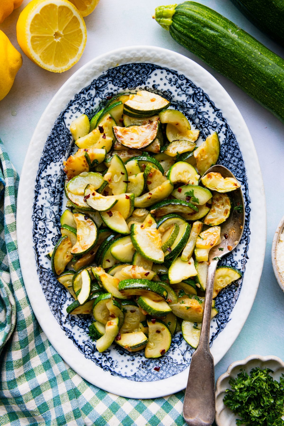 Overhead shot of sauteed zucchini on a blue and white serving platter with a green and white check cloth napkin.