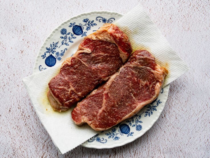 Patting steaks dry after marinating.
