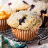 Horizontal side shot of a sour cream blueberry muffin on a cooling rack.